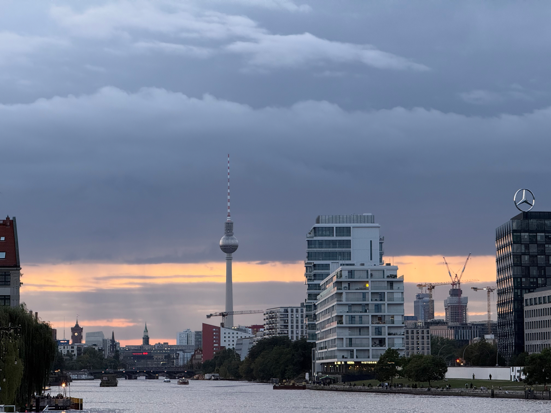 Die Skyline von Berlin über der Spree bei Sonnenuntergang mit dem Roten Rathaus und dem Fernsehturm und mehreren modernen Gebäuden Unter dramatischen Wolken ist zu sehen.